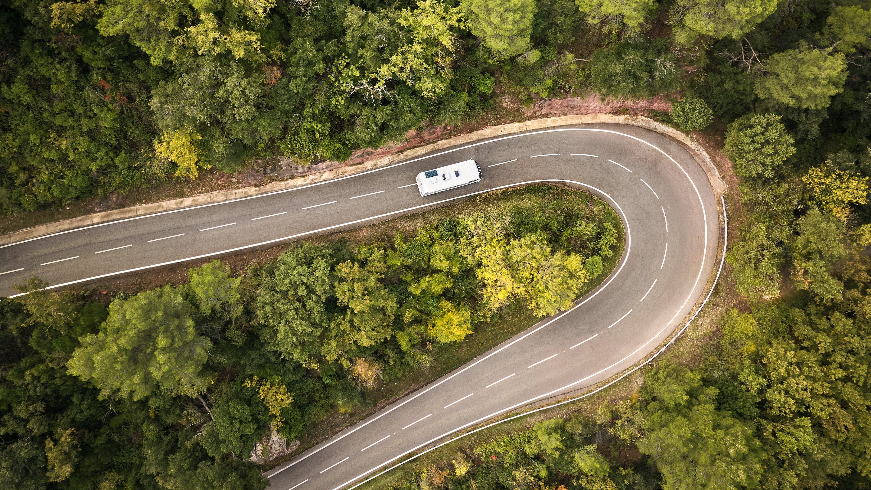 Aerial view of a motorhome driving along a winding road through a forest landscape, showcasing road travel and outdoor adventure