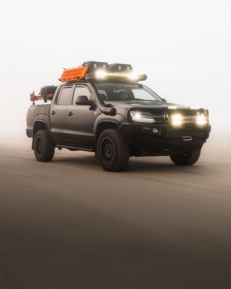 Pickup truck equipped with a roof rack, LED light bar, recovery boards and storage boxes driving in dusty off-road conditions