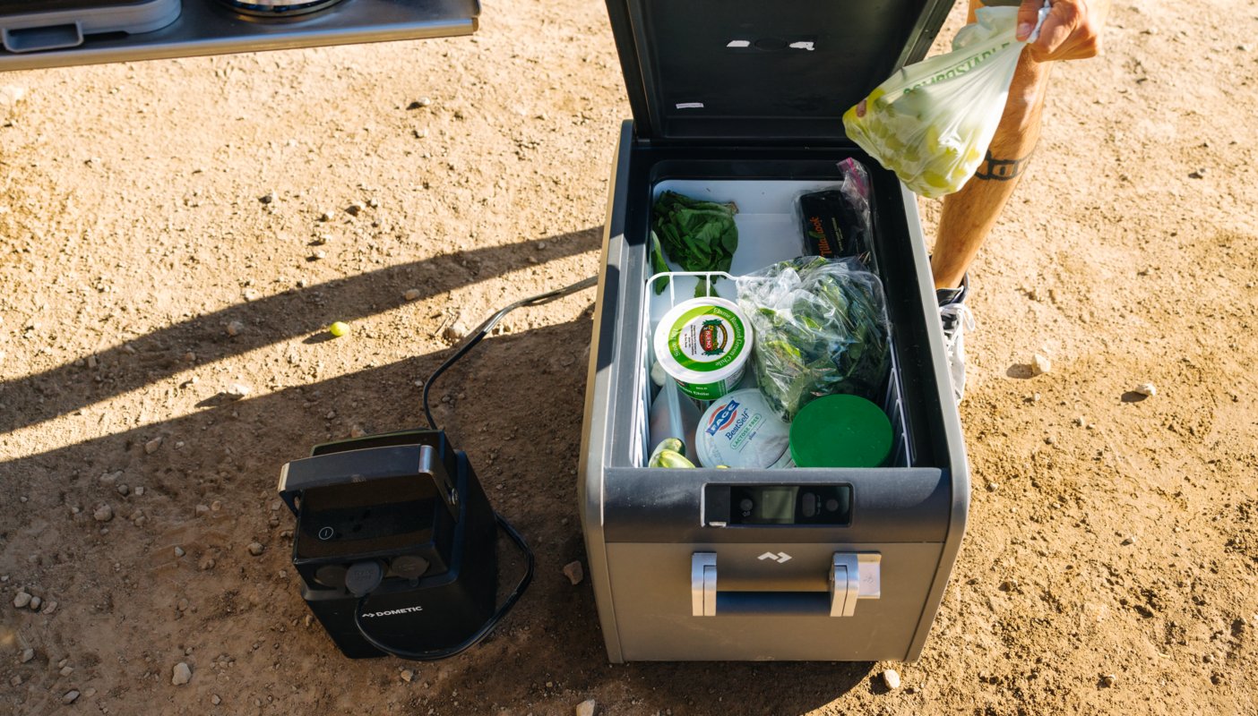 Öppen Dometic CFX5 kompressorkylbox med färsk mat utomhus på sandig mark