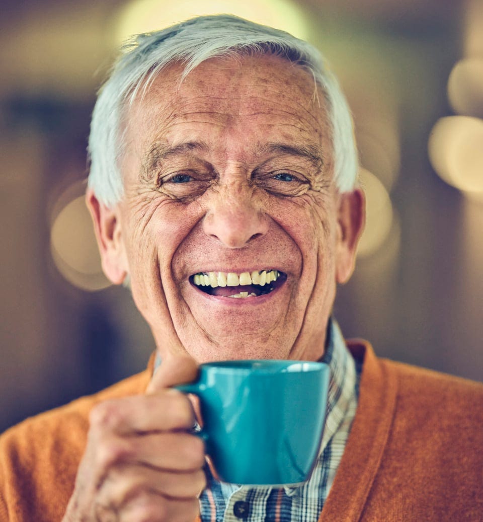 Elderly man smiling with a cup of coffee in his hand