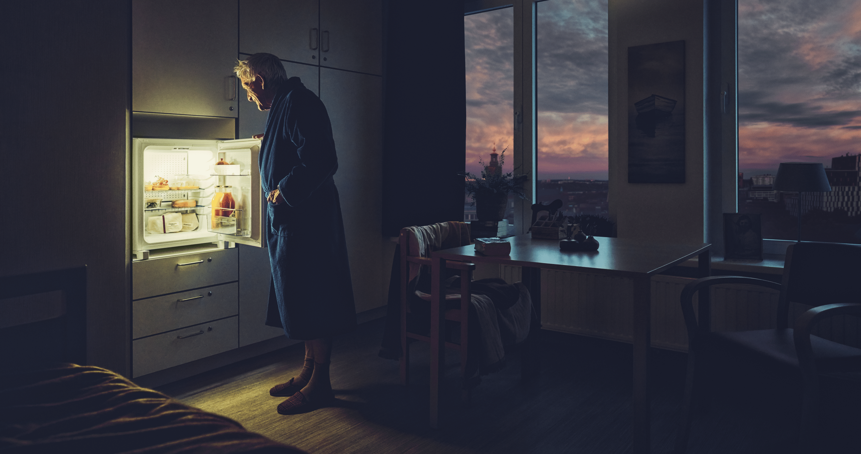 Elderly gentleman looking inside a fridge in a nursing home room at night