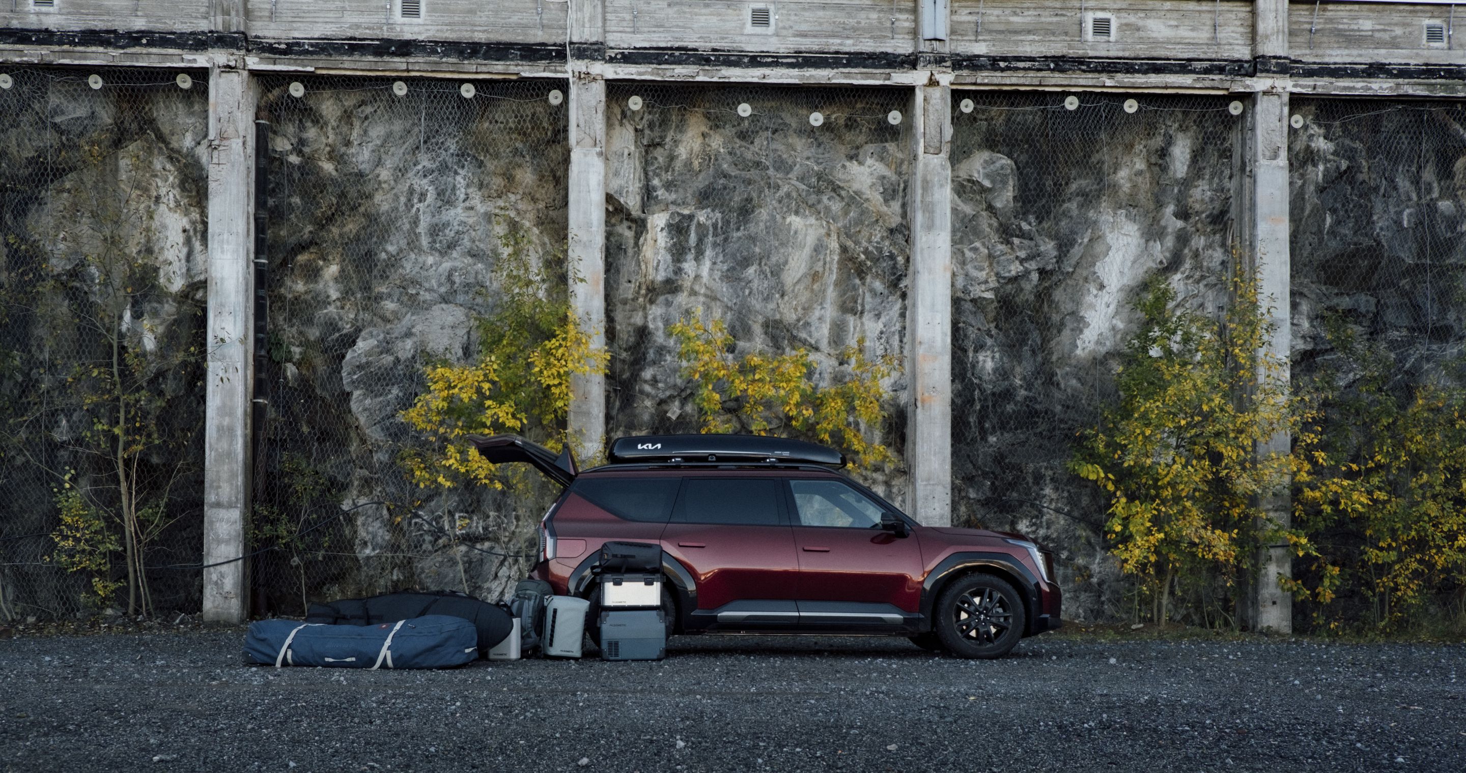 A SUV parked against a rugged rock wall with the boot open, surrounded by outdoor gear and adventure ready.