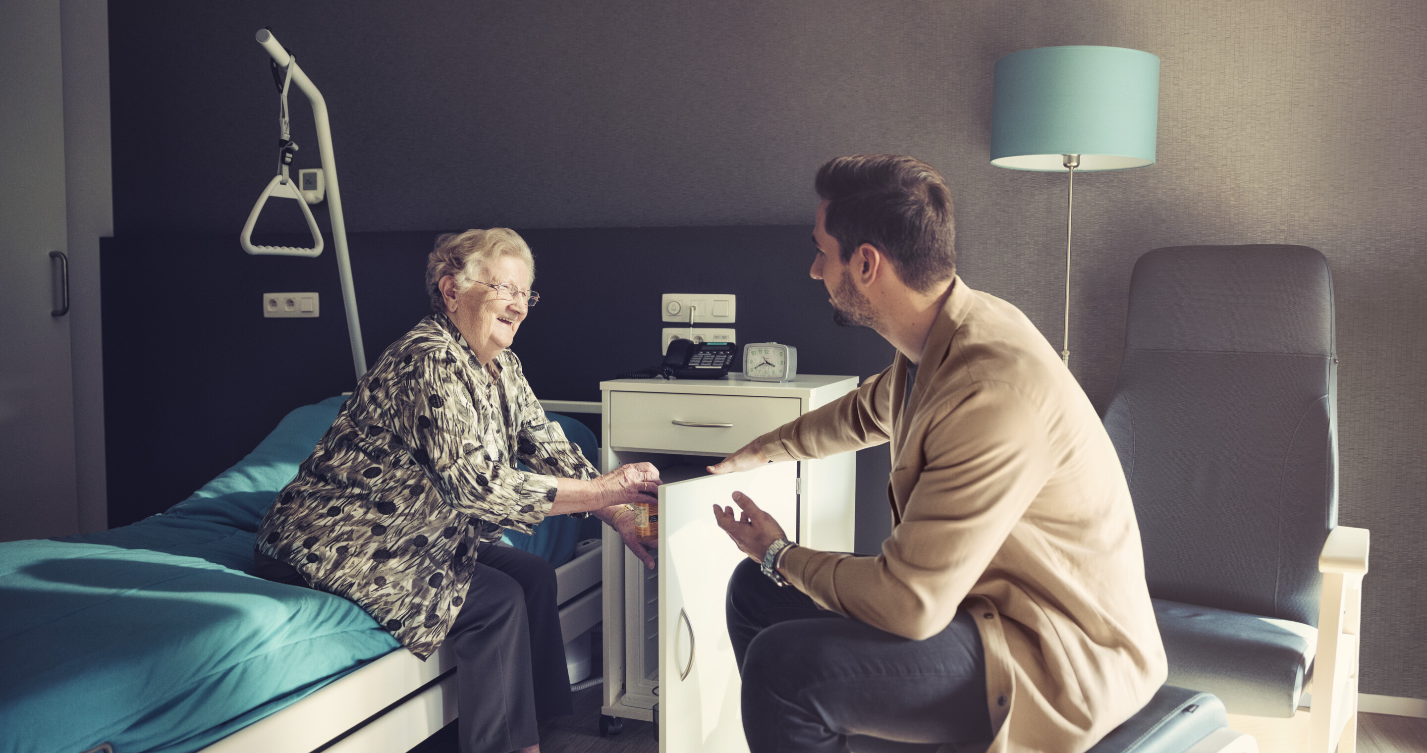Nurse and elderly man smiling at eachother in a care room