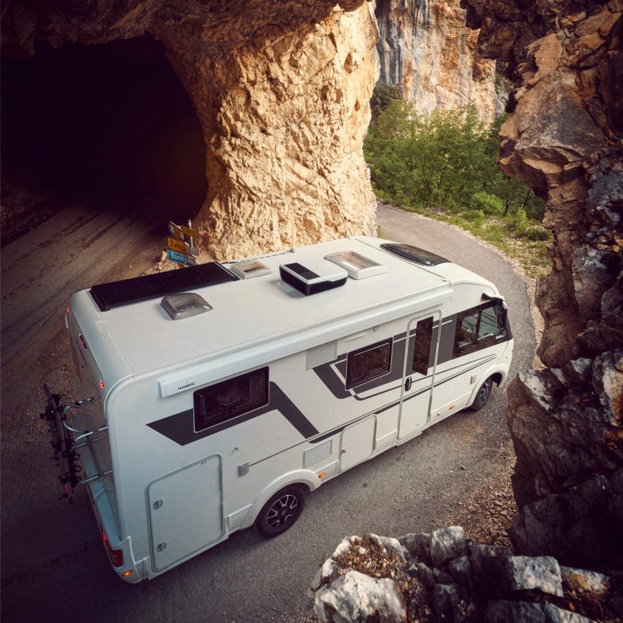 Motorhome driving along a scenic mountain road near a rocky tunnel — ideal for road trip adventures and RV travel inspiration.