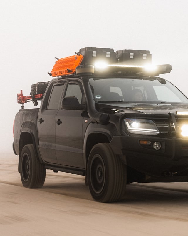 Off‑road vehicle with a roof rack and side‑mounted shower or privacy enclosure in an outdoor setting.