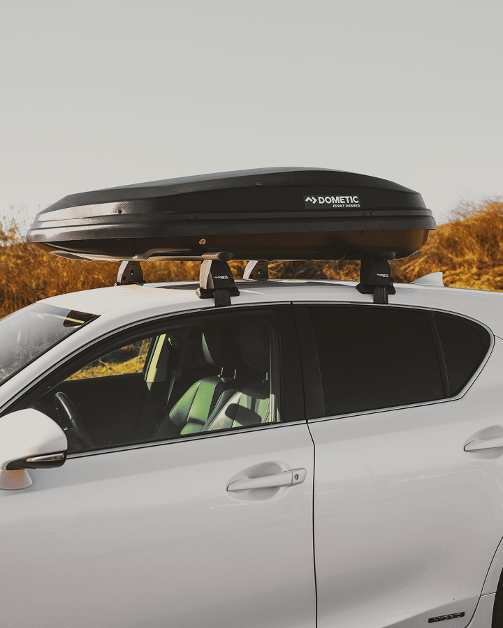 Véhicule équipé de barres de toit portant un coffre de toit en extérieur.