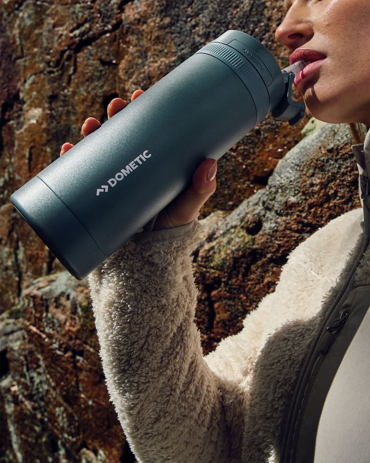 Blå isolerad termoflaska som hålls utomhus framför en klippvägg.