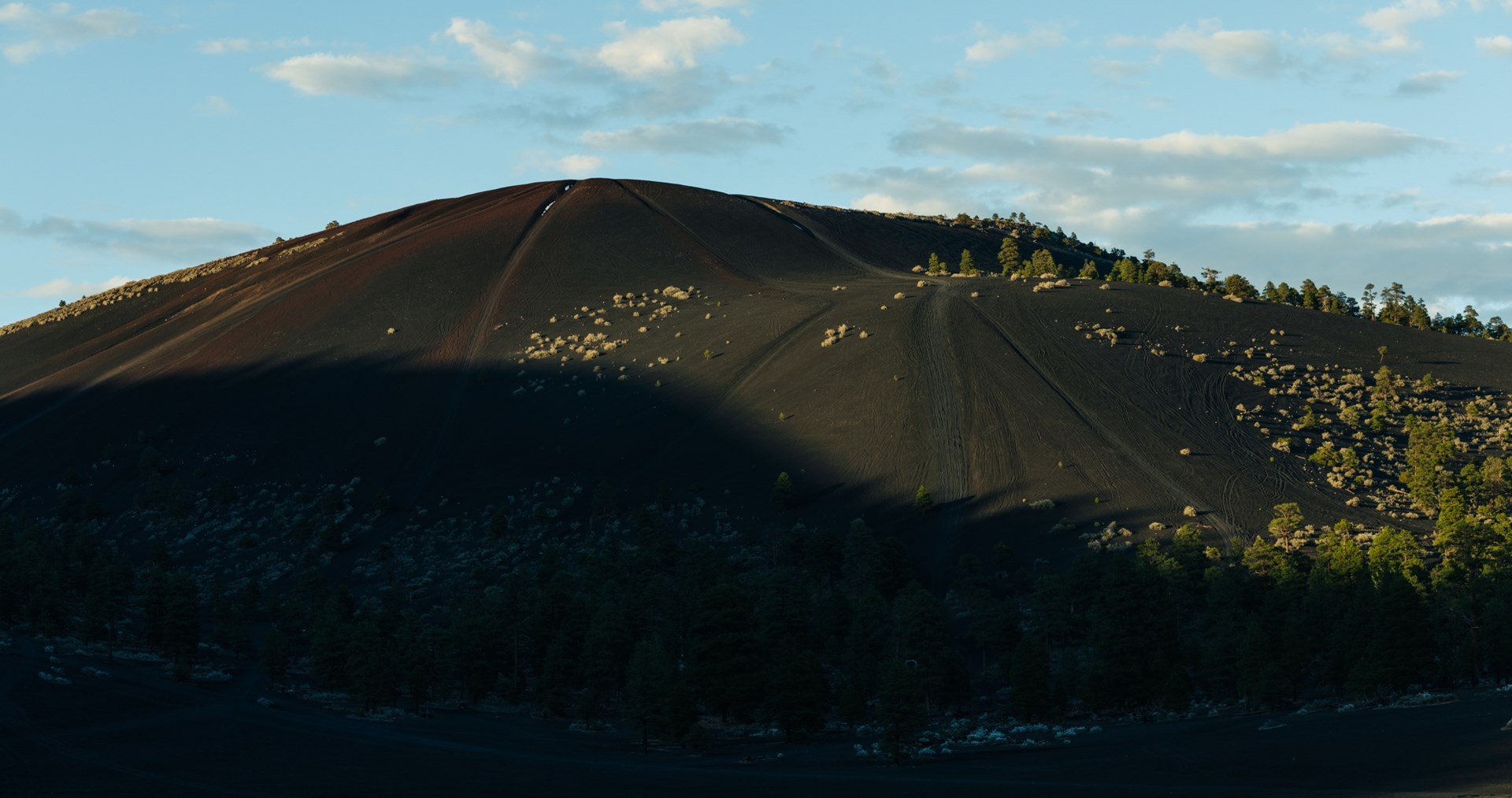 Alpine landscape at sunset with dark slopes and pine forest – stunning mountain scenery.