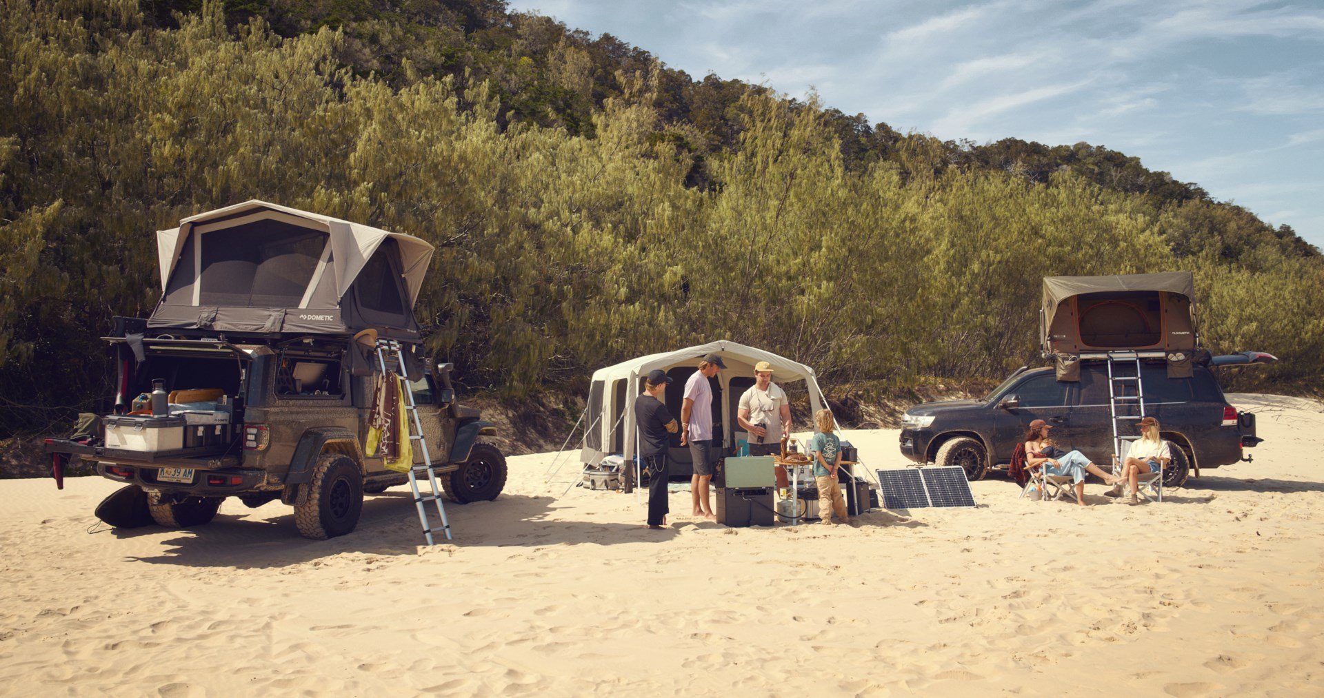 Familiencamping am Strand mit Dachzelten, Kühlboxen und Solarpanels in der Sonne