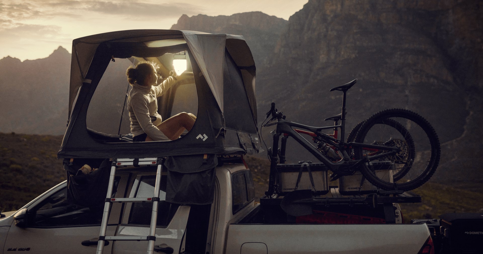 Woman in rooftop tent as the sun is setting in the background