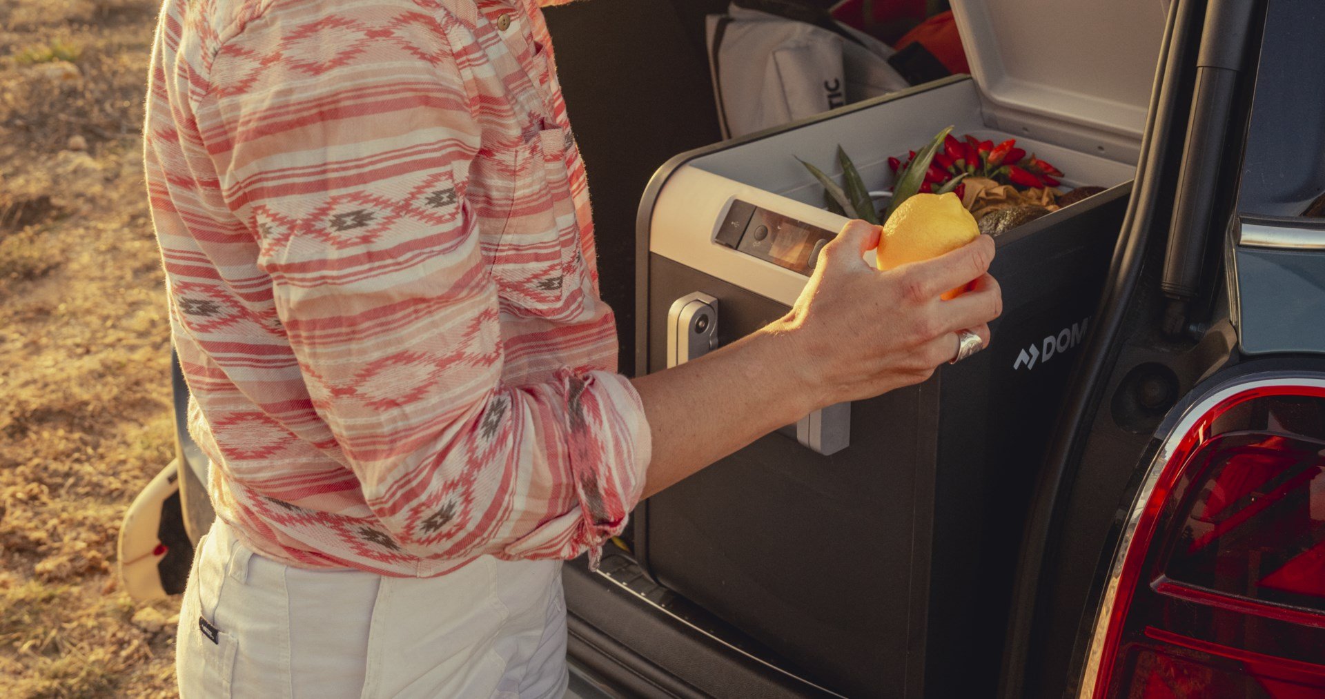 Woman opening Dometic CFX3 cooler from trunk of car