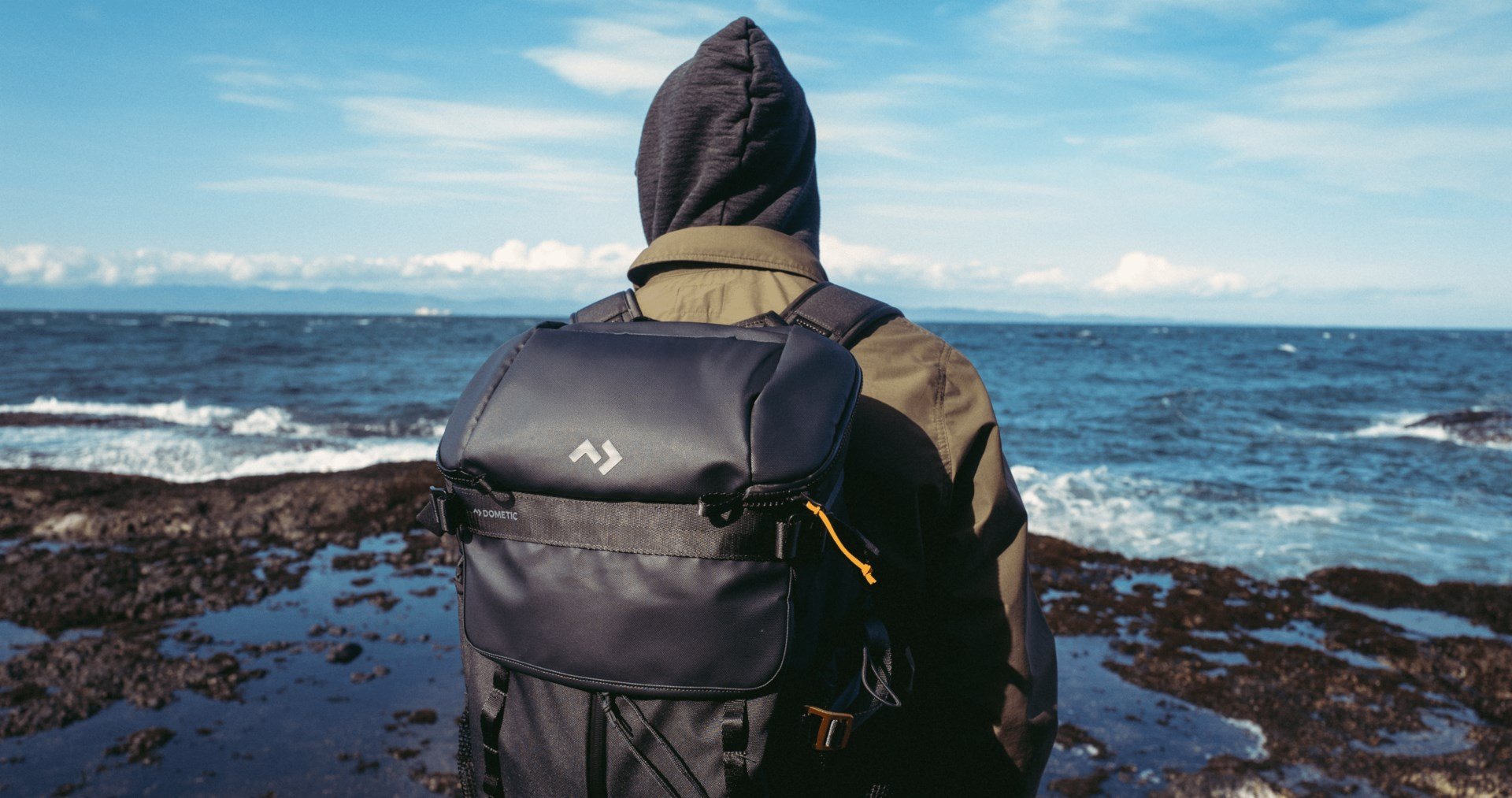Persona con chaqueta con capucha y mochila nevera Dometic Unrestricted junto a una costa rocosa