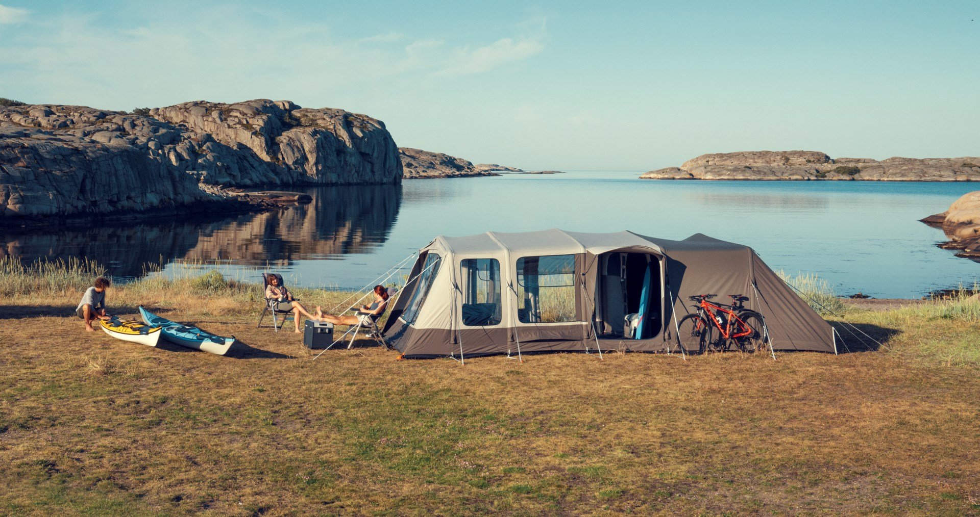 Coppia rilassata fuori dalla tenda sulla costa con attrezzatura da campeggio Dometic, inclusi un frigorifero a compressore CFX e arredi da campeggio.